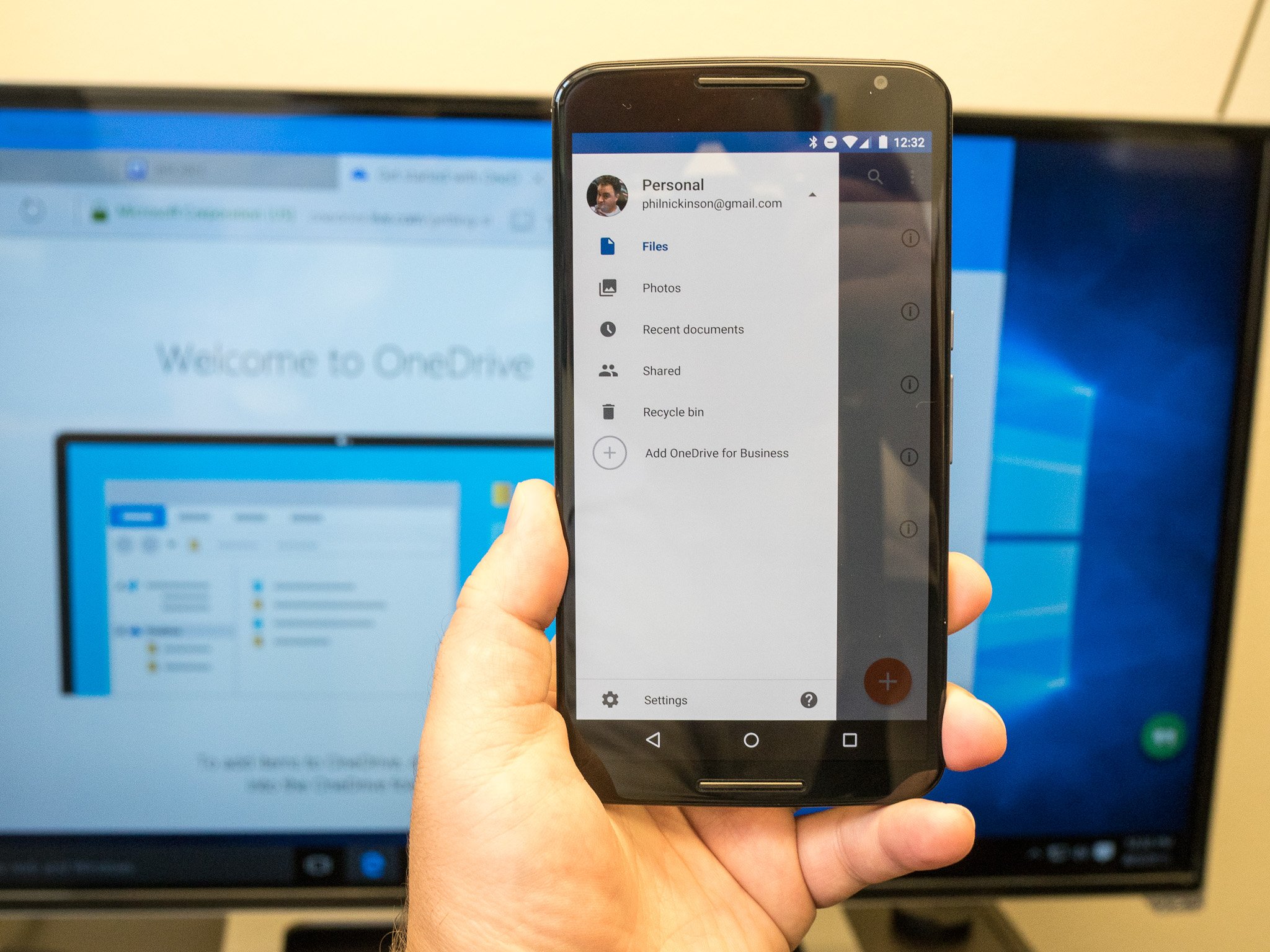 A phone held in front of a PC monitor, both showing the Microsoft OneDrive app