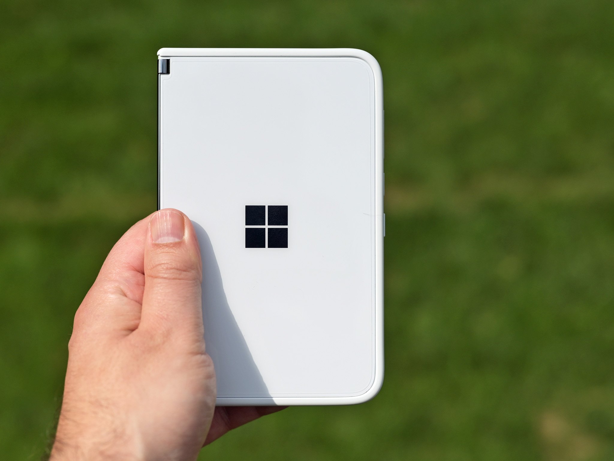 Surface Duo held up against a green, leafy backdrop